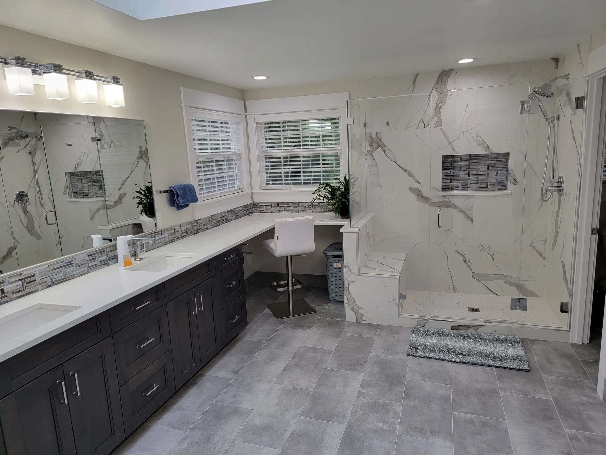 Large master bathroom with dark cabinets, quartz countertop, marble-look porcelain shower walls, mosaic accent niche, and accessible open shower