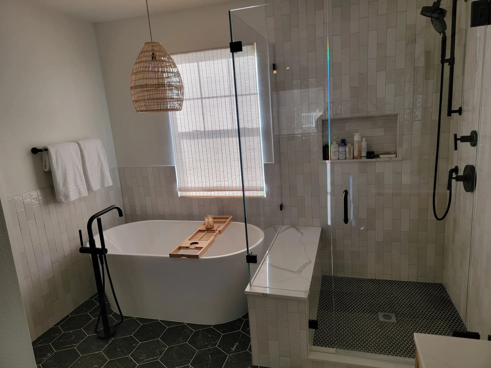 Master bathroom with freestanding tub, dark hexagonal floor tile, walk-in shower with bench and zellige tile, woven pendant light, and black fixtures