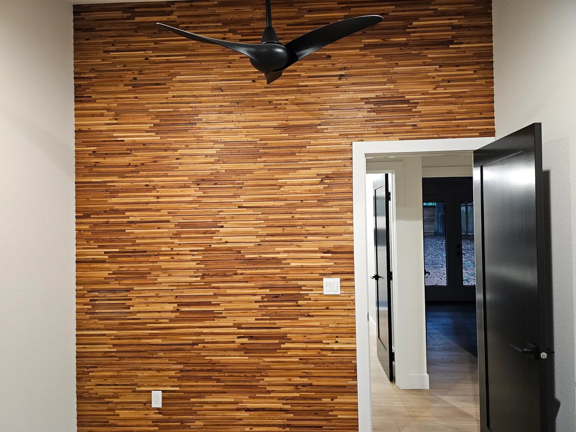 Accent wall with horizontal teak strip tile in varied tones, modern sculptural ceiling fan, and doorway