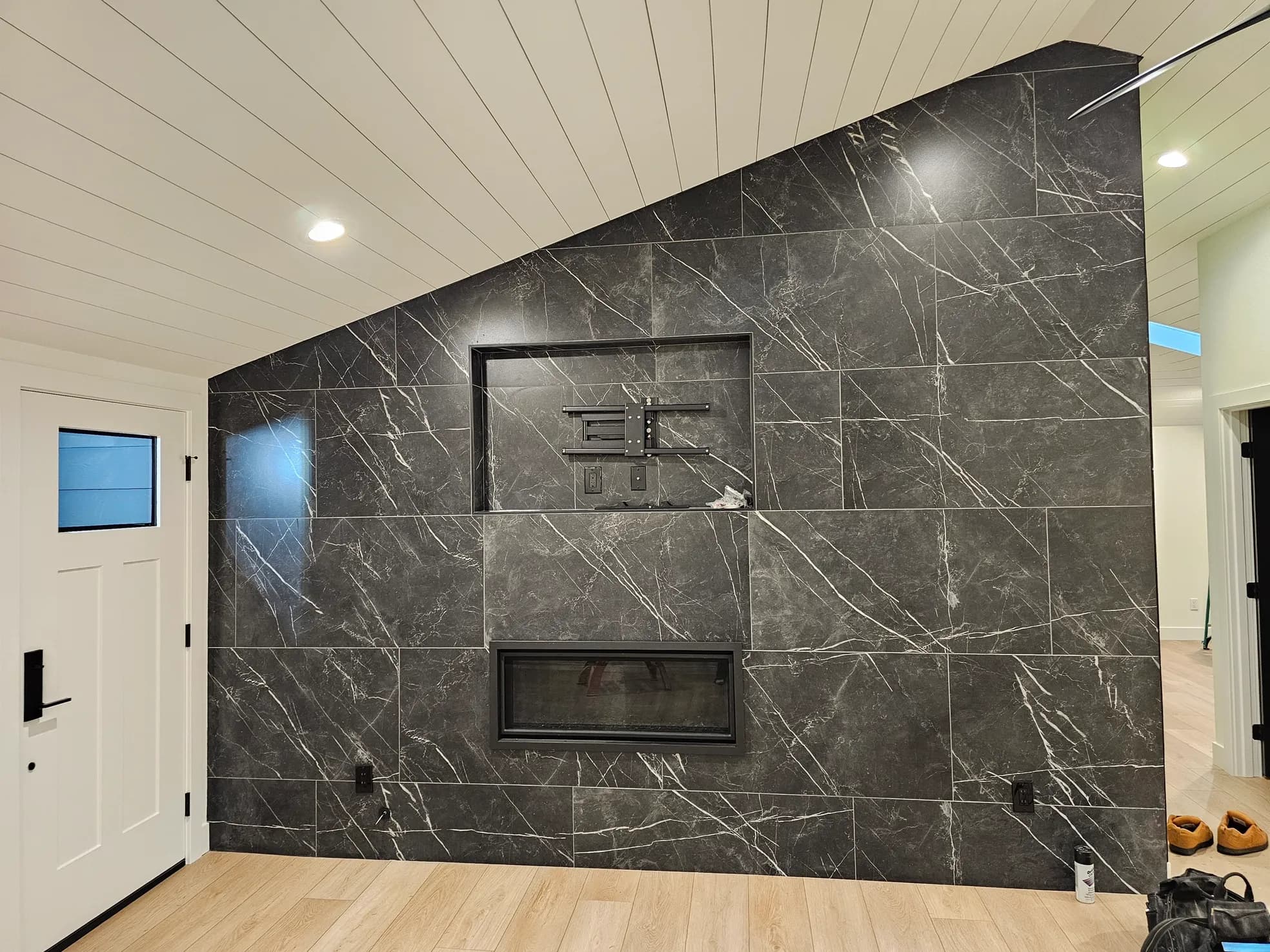 Living room accent wall with large-format dark marble tile floor to vaulted ceiling, TV mount, and linear fireplace with shiplap ceiling