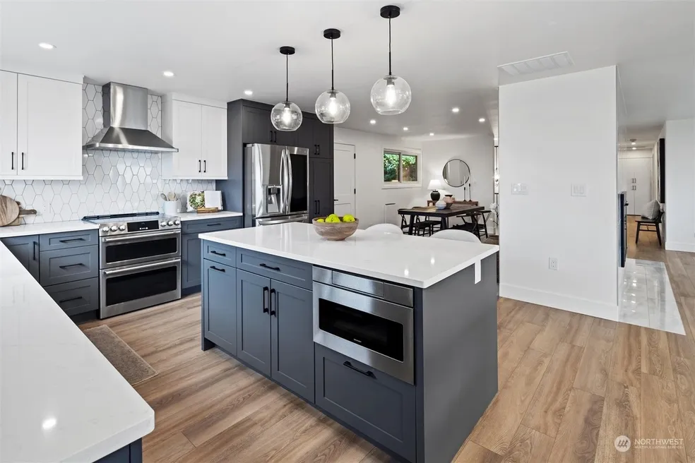 Kitchen with navy-grey island, white upper cabinets, hexagonal tile backsplash, glass pendant lights, and quartz countertops