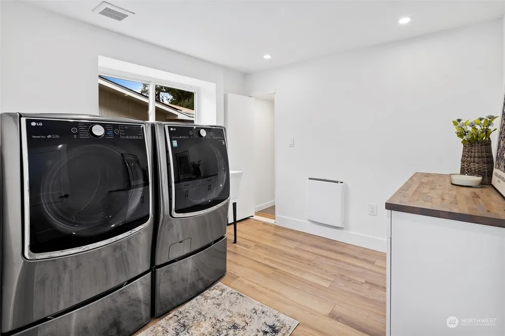 Laundry room with LG front-load washer and dryer on pedestals, butcher block counter, and hardwood floors