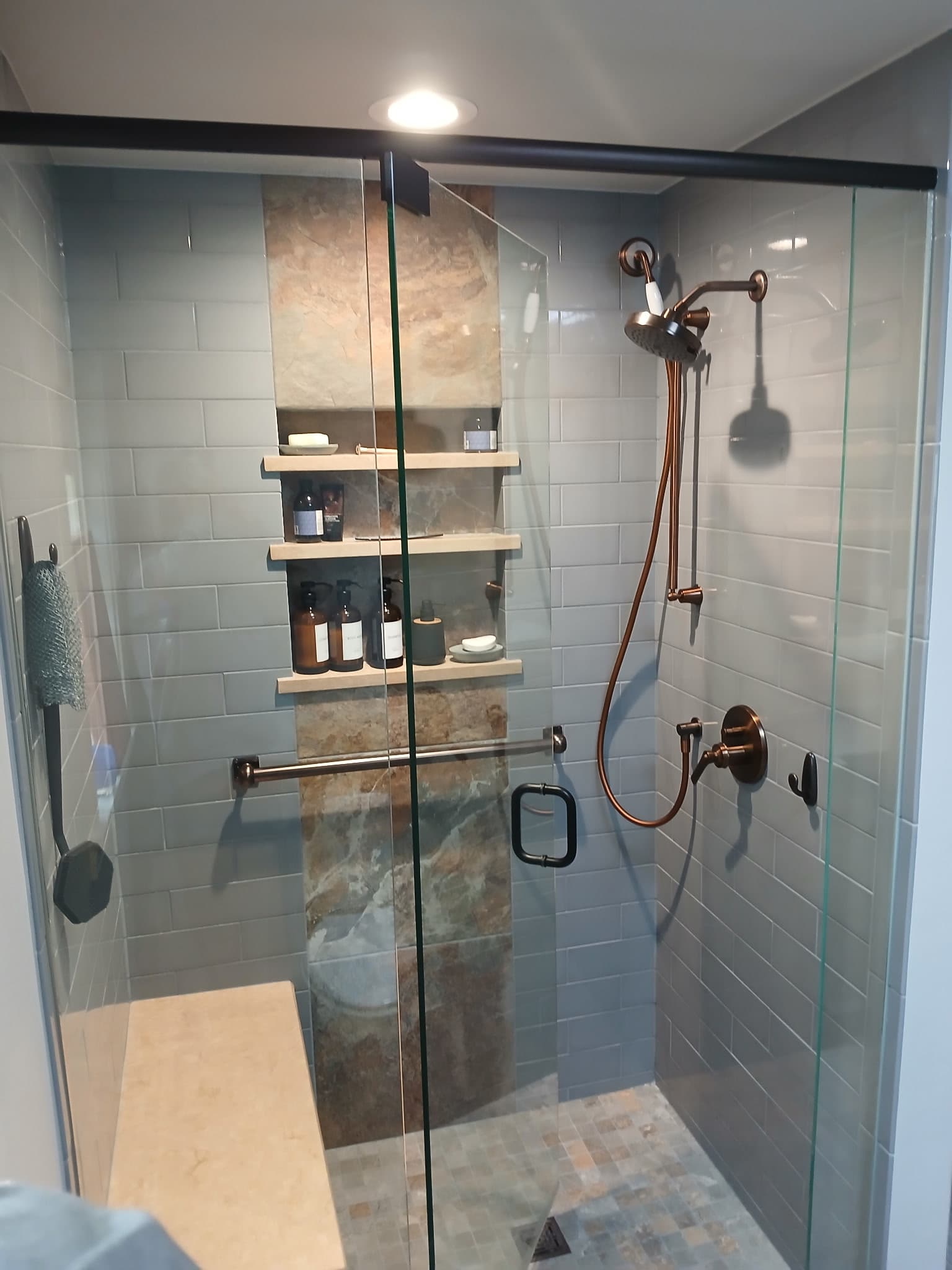 Bathroom shower with sage subway tile, stone accent niche, and copper fixtures