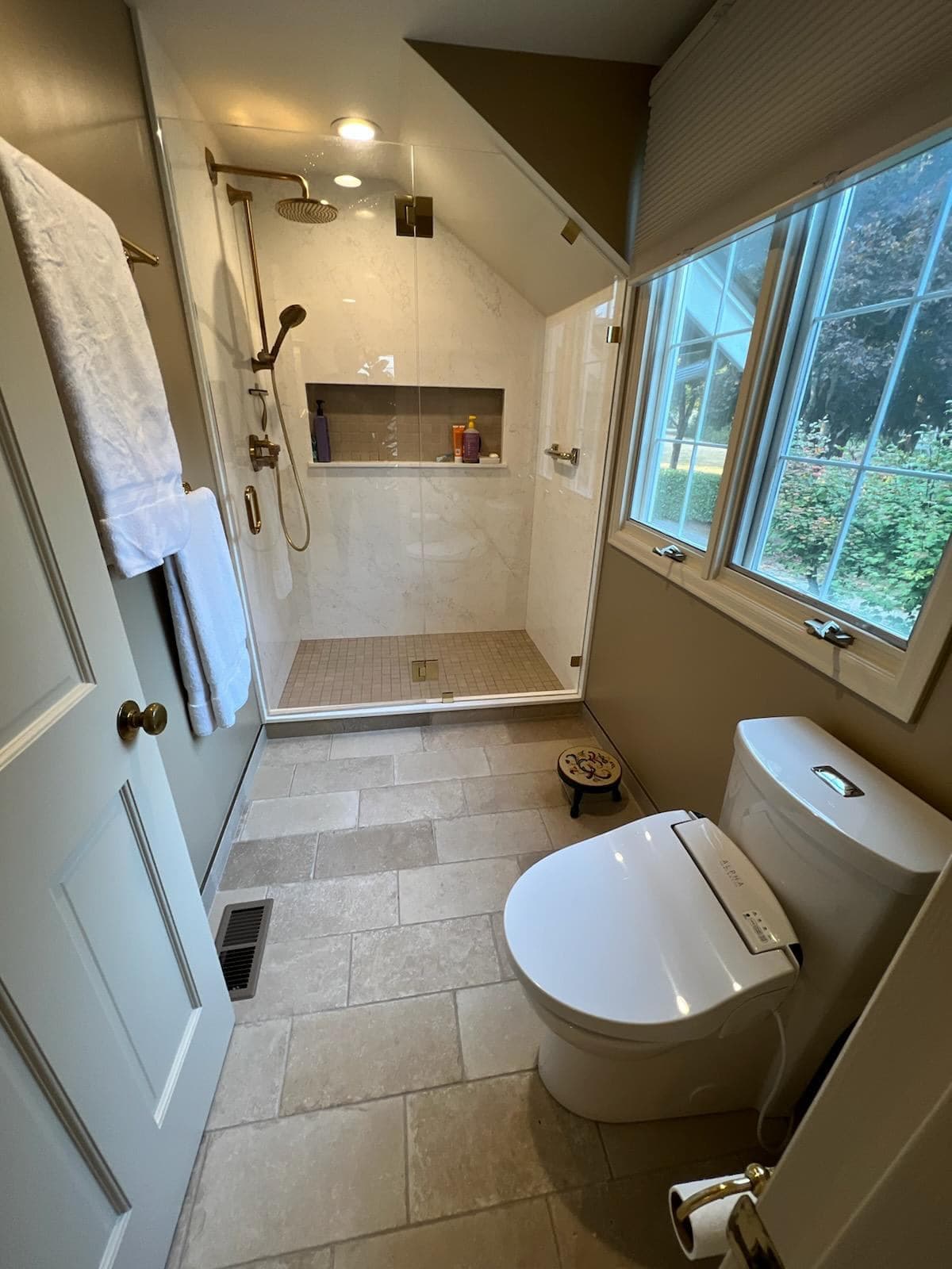 Bathroom with walk-in shower under sloped ceiling, brass fixtures, and glass enclosure