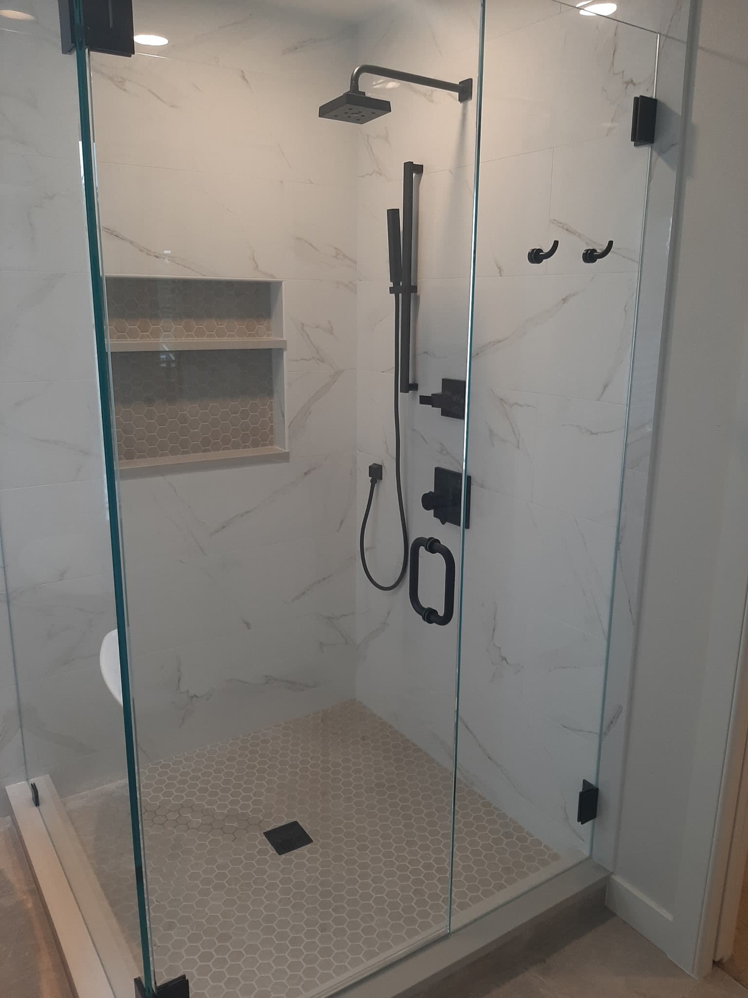Walk-in shower with marble-look tile, frameless glass enclosure, black fixtures, and hexagonal floor tile