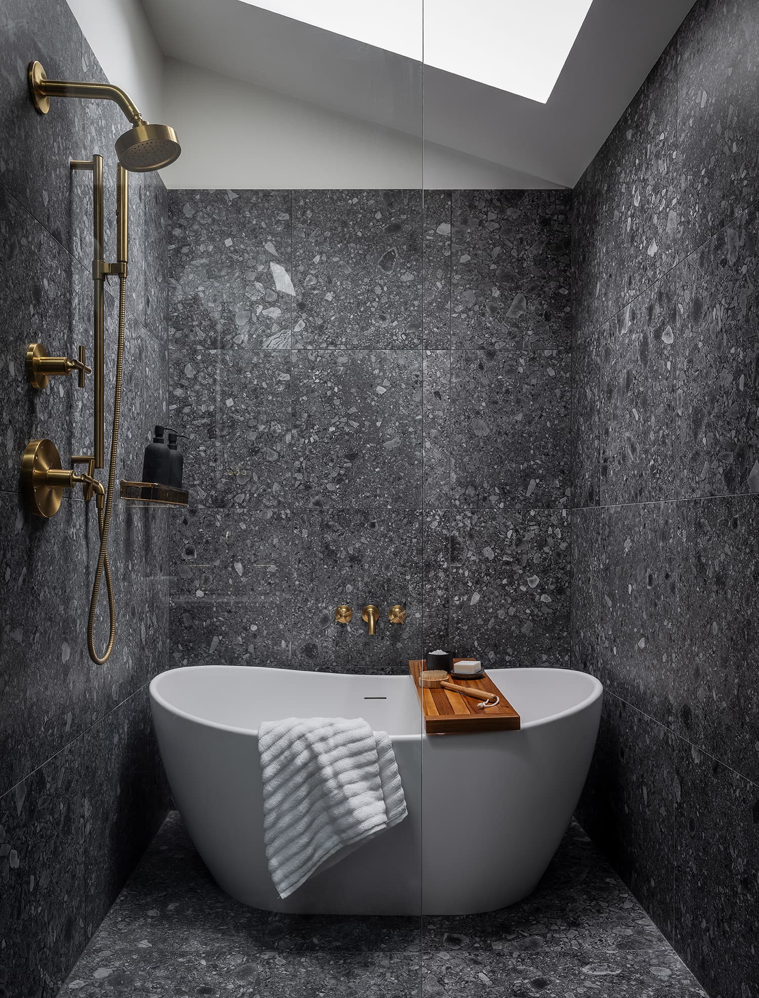 Master bathroom with freestanding soaker tub, stone walls, skylight, and brass shower fixtures