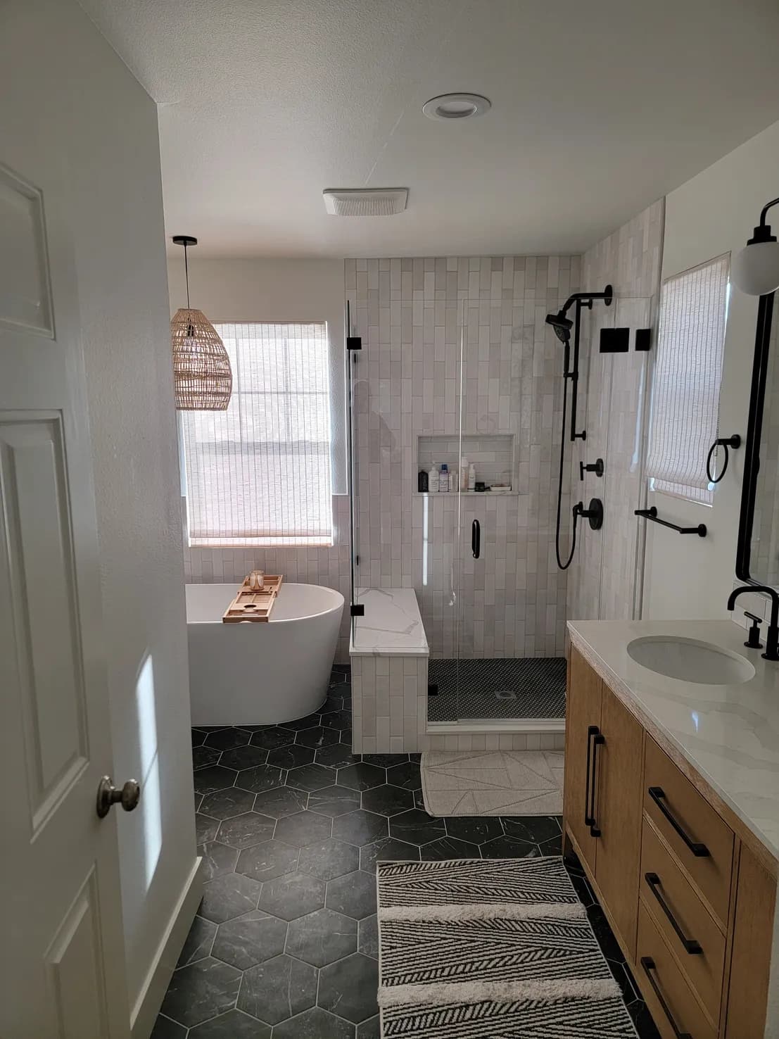 Master bathroom from wider angle showing freestanding tub, walk-in shower with glass enclosure, light wood vanity, and dark hexagonal floor tile
