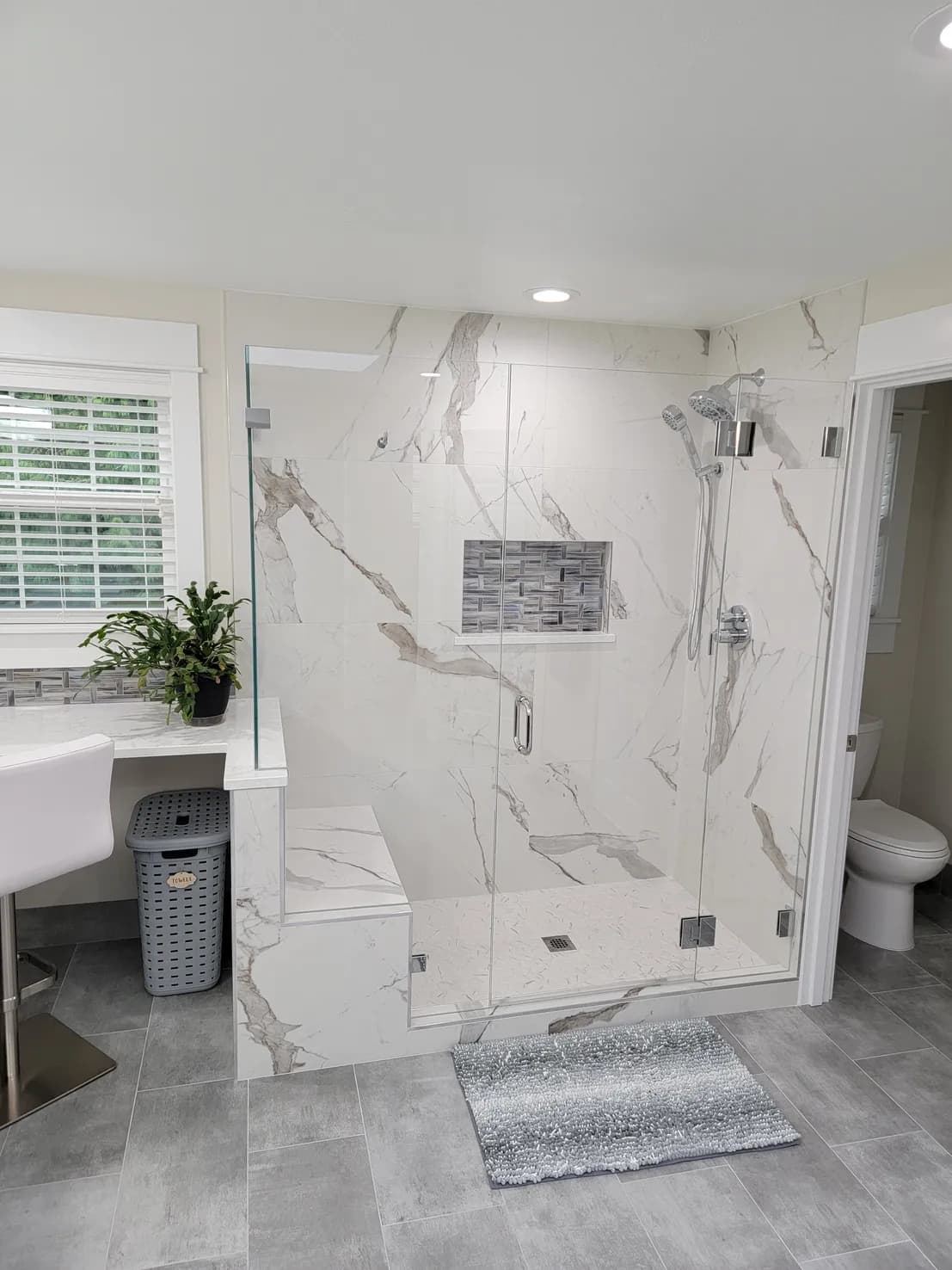 Walk-in shower with marble-look porcelain slab walls, frameless glass enclosure, mosaic tile accent niche, and chrome fixtures