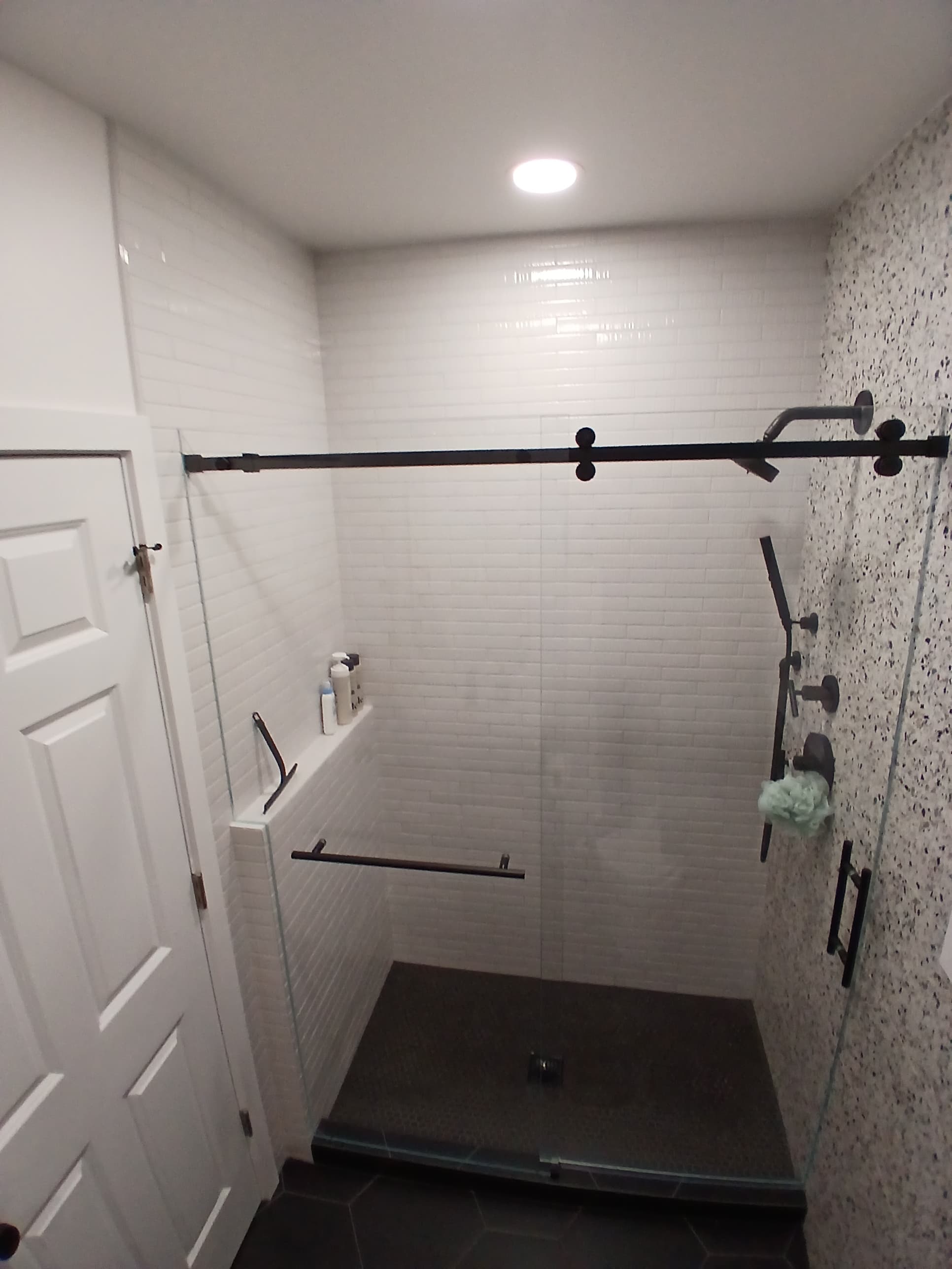Walk-in shower with white vertical stacked tile walls, terrazzo ceiling, black fixtures, and frameless glass panel