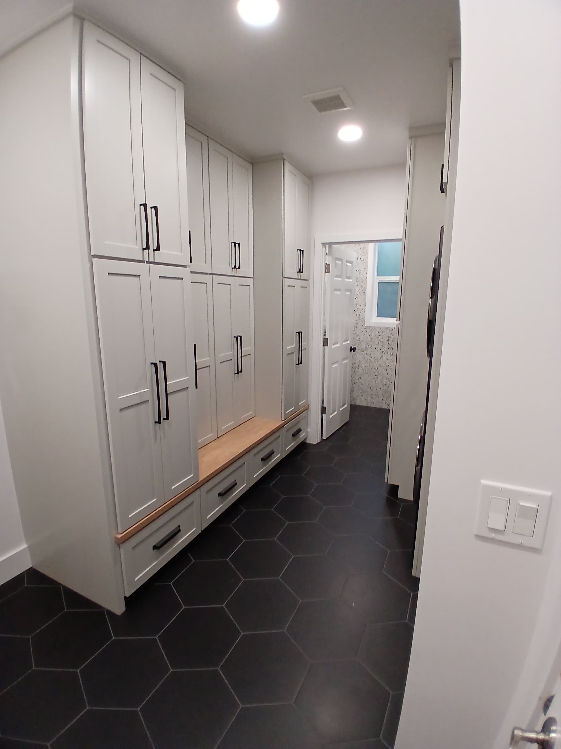 Mudroom with white shaker cabinets, dark hexagonal floor tile, terrazzo backsplash accent, and black hardware