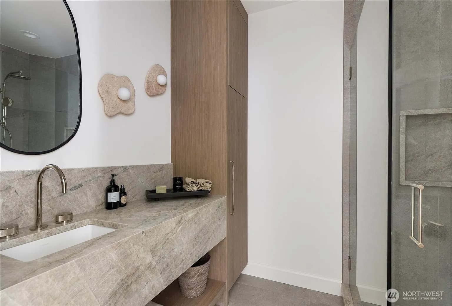 Guest bathroom with marble vanity, round mirror, sculptural sconces, and glass shower